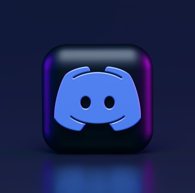 A 3D-style block with a blue logo in the center, set against a dark background. The logo resembles a game controller with two rounded edges and two circles on the front. The block has a subtle gradient, transitioning from dark to purple on its sides.